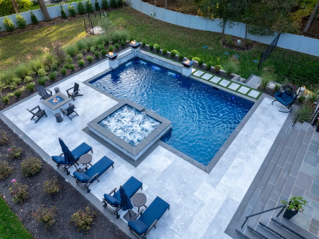 Angled aerial view of pool, raised spa, fire table, loungers, and landscaping