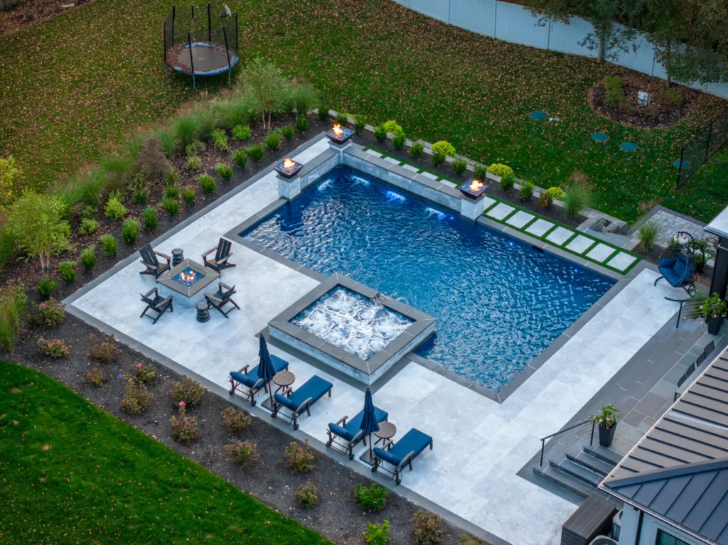 Aerial view of pool, raised spa, fire bowls, patio seating, and landscaped yard