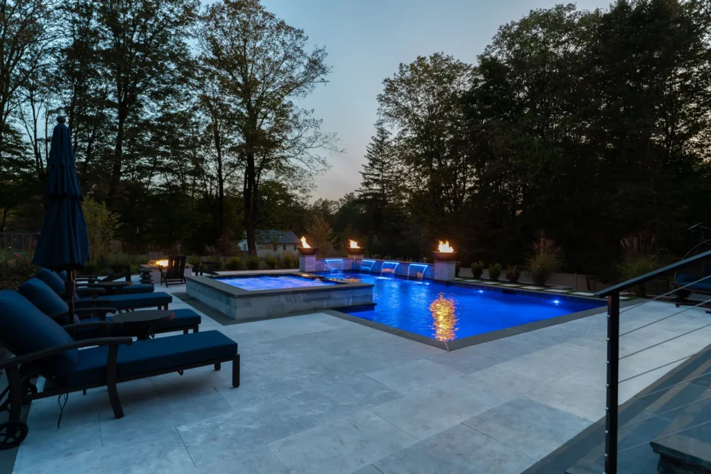 Blue-lit pool and raised spa with fire bowls and waterfalls at dusk