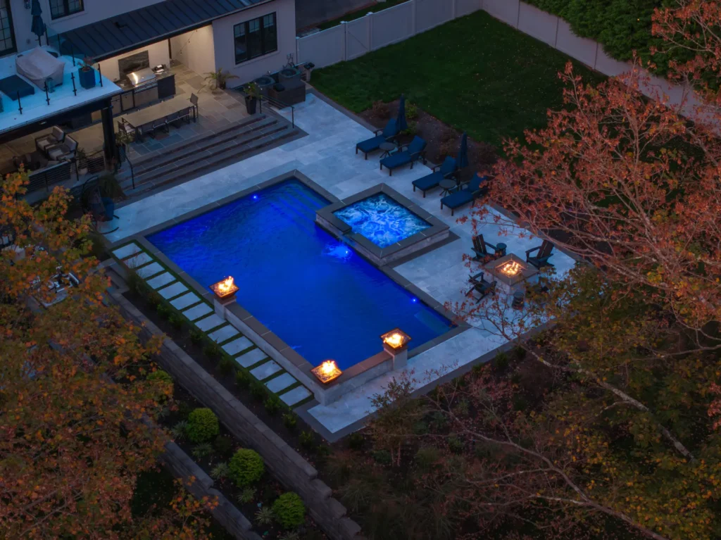 Twilight aerial view of a blue-lit pool, raised spa, fire features, and patio
